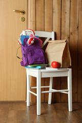 Backpack with school supplies on chair on wooden background