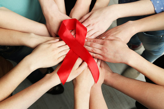 Group of female hands with red ribbon as breast cancer awareness symbol, closeup
