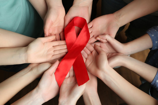 Group of female hands with red ribbon as breast cancer awareness symbol, closeup