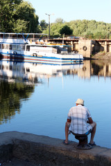 Fototapeta na wymiar fisherman fishing in the city river near motor ship