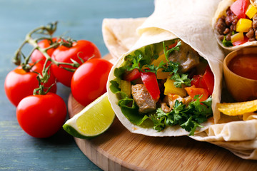 Homemade tasty burrito with vegetables, potato chips on cutting board, on wooden background