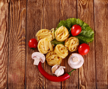 pasta on the wooden background with tomato, pepper, olive oil, mushrooms and lettuce