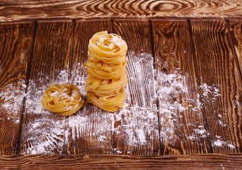 Pasta (tagliatelle) and flour on wooden surface.