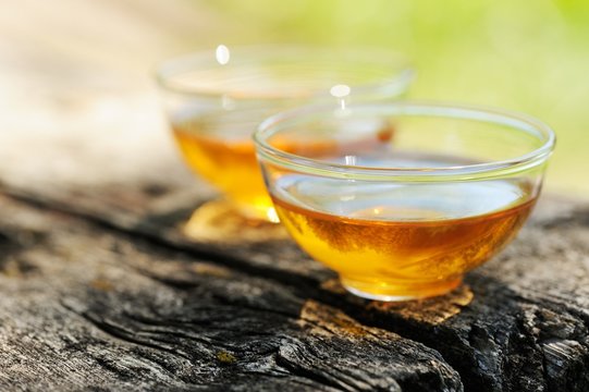 Two transparent cups of black tea on old wooden board in bright