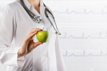 Doctor's hand holding green apple on blurred medical background