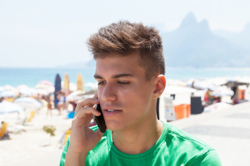 Fototapeta na wymiar Tourist im grünen Shirt mit Telefon am Strand