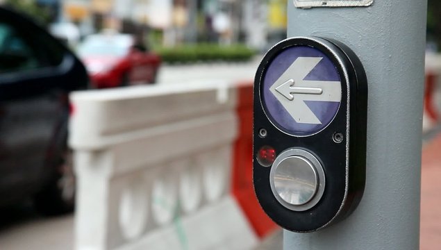 hand presses the button on the pedestrian crossing