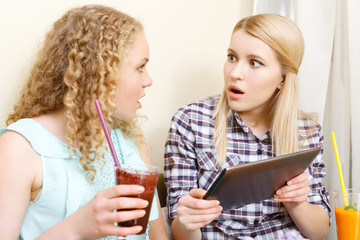 Two amazed girls with tablet in cafe