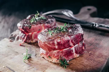 Crédence de cuisine en verre imprimé Viande Filets de steak de chevreuil assaisonnés rares sur planche de bois