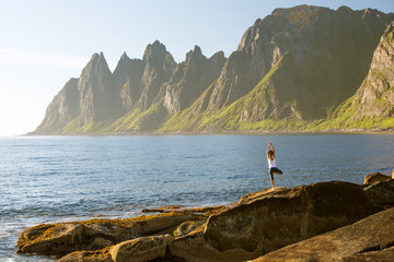 Fototapeta na wymiar Young woman is practicing yoga between mountains in Norway