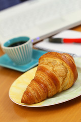 Croissant and black coffee on office desk
