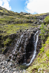 Large mountain waterfall in the Lake District with water flowing down the rocky hillside and green grass