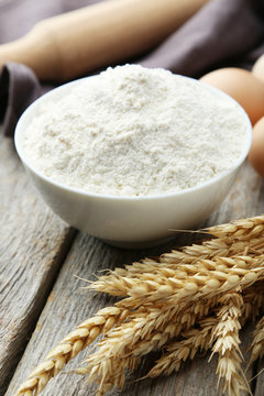 Bowl of wheat flour with spikelets on grey wooden background