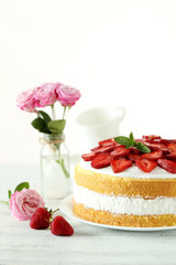 Sweet cake with strawberries on plate on white wooden background