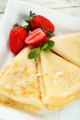 Pancakes with strawberry on plate on white wooden backgound