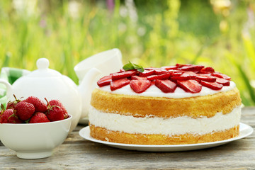 Sweet cake with strawberries on plate on grey wooden background