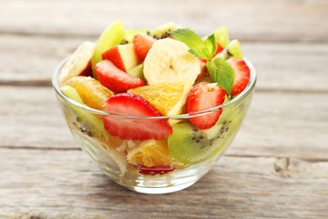 Fresh fruit salad in bowl on grey wooden background