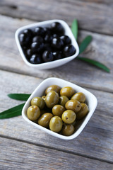 Green and black olives in bowl on grey wooden background