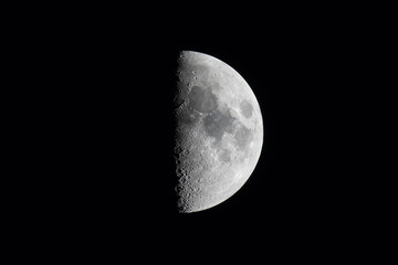 Half moon or first quarter phase in a black sky. - obrazy, fototapety, plakaty