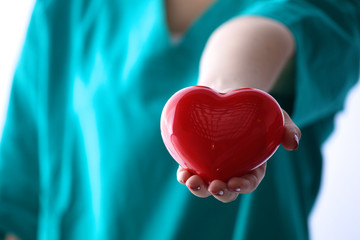 Female doctor with stethoscope holding heart over white