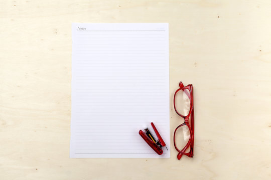 White note on wood background with red eyeglasses and stapler