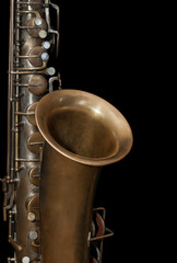 Fragment of a vintage saxophone on black background