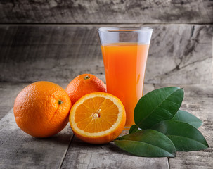 Orange juice glass and fresh oranges on wood