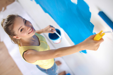 Happy beautiful young woman doing wall painting, standing on