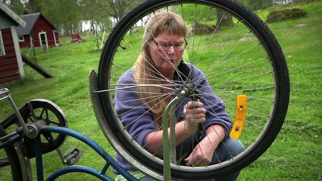 Woman is mending an old bike outdoors.