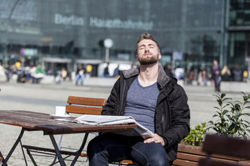 Attraktiver Mann sitzt in einem Cafe und geniesst die Sonnenstrahlen
