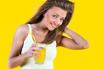 Teenager girl drinking orange juice on yellow background