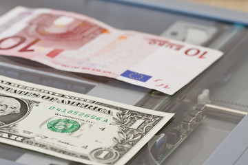 Denominations of one dollar and ten euros lie on scaner