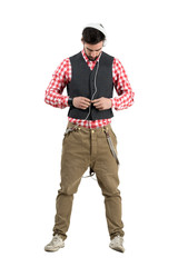 Young bearded man buttoning waistcoat wearing earphones 