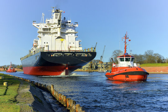 A orange tugboats assisting a large oil tanker.