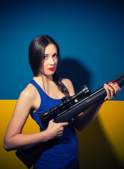 Fototapeta na wymiar beautiful young woman posing with rifle against blue and yellow