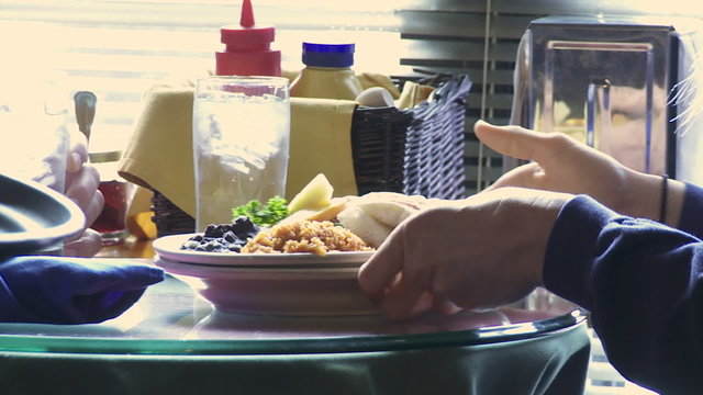 Detail of a restaurant server's hand placing brunch in front of a diner.