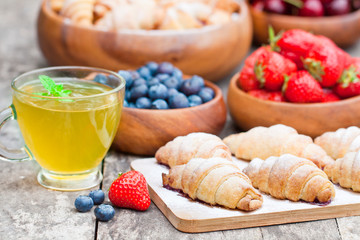 fresh croissants and berries with cup of fruit tea on old table