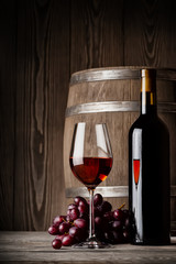 Obrazy na Szkle  Kieliszek czerwonego wina ze stojącą butelką i beczką