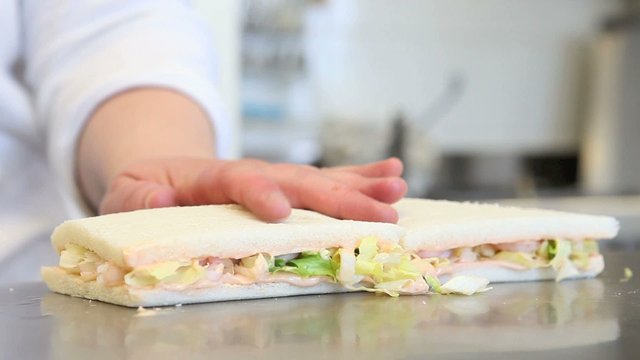 Hands cutting a sandwich with shrimp and lettuce