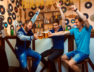 men celebrate in the bar and clink glasses with beer