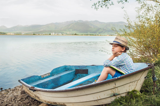 Dreaming boy in old boat at the lake coast
