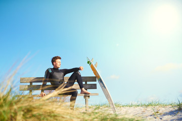 Surfer relaxing on a wooden bench on a dune