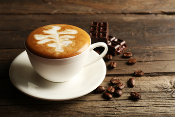Cup of coffee latte art with grains and chocolate on wooden background