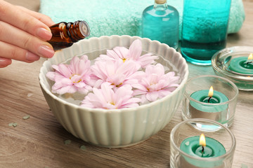 Female hand with bottle of essence and bowl of aroma spa water on wooden table, closeup