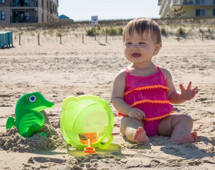 Baby girl tasting sand on beach