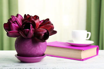 Beautiful tulips in pot with book on fabric background