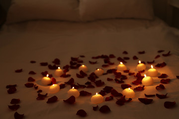 Heart of candles and red petals on bed, close up