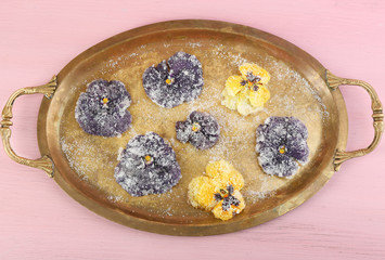 Candied sugared violet flowers on tray, on color wooden background