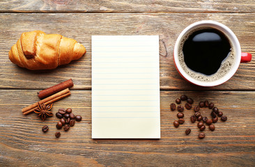 Cup of coffee with fresh croissant and blank sheet of paper on wooden table, top view