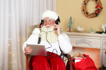 Santa Claus sitting with Digital tablet in comfortable chair near fireplace at home